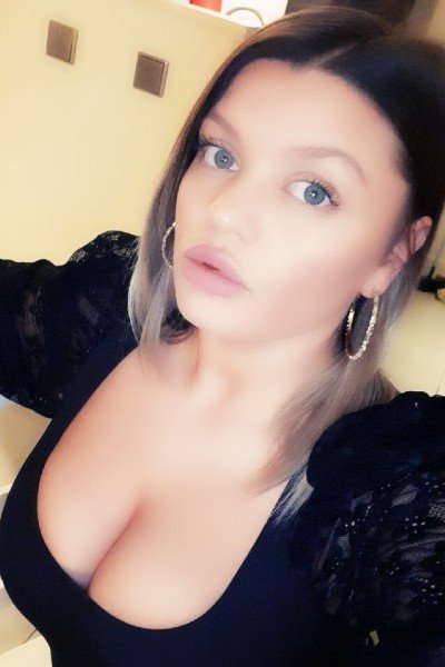 Alina taking a selfie in a black dress that shows her large cleavage.
