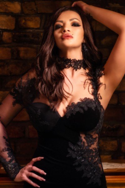 Victoria in her short black dress, she stares at you with an intense look and has one hand on her hip.